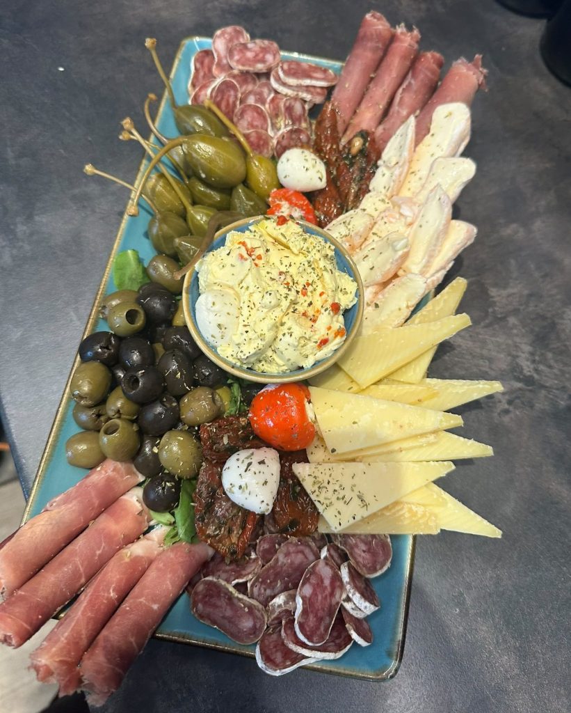 Antipasti-Platte mit Schinken, Salami, Käse, Oliven, getrockneten Tomaten und Kräuterdip