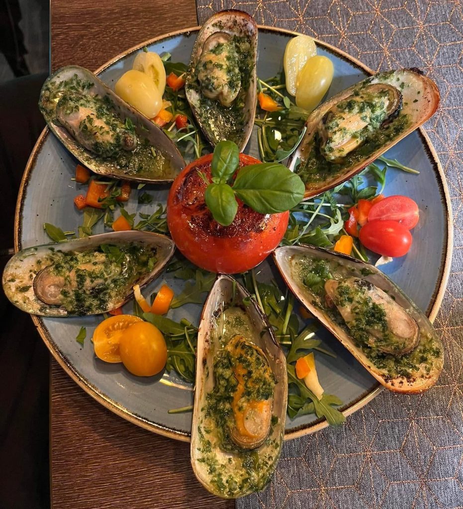 Überbackene Muscheln mit Kräuteroel, angerichtet mit Rucola, Tomaten und Basilikum