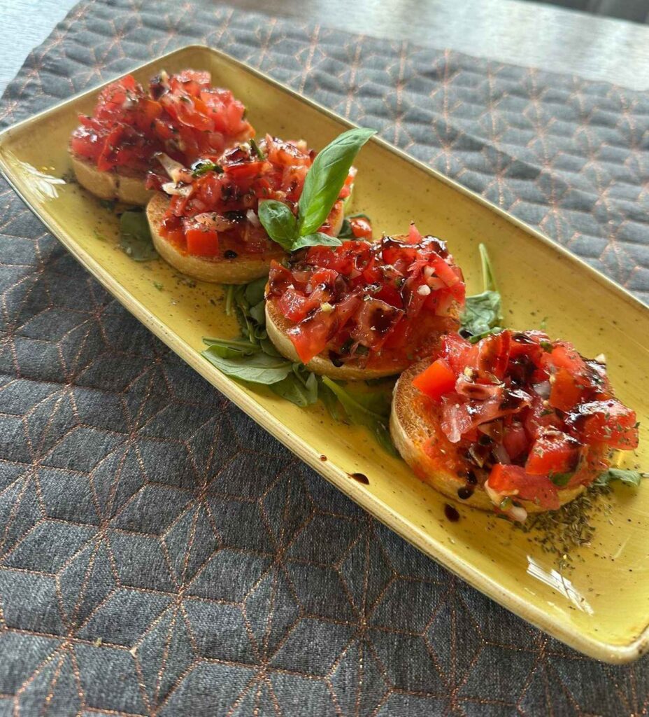 Vier Scheiben Bruschetta mit Tomaten, Basilikum und Balsamico-Reduktion auf gelbem Teller