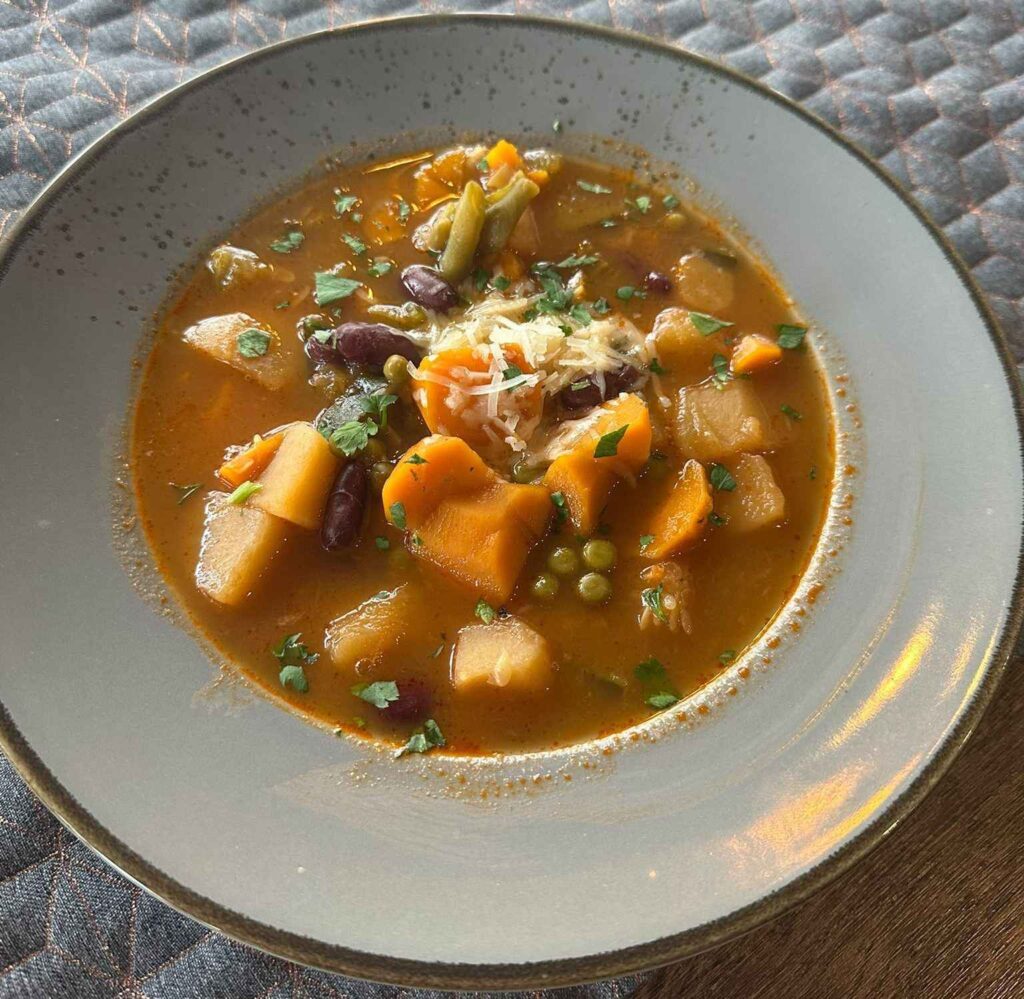 Minestrone-Suppe mit Kidneybohnen, Karotten, Kartoffeln, Erbsen und geriebenem Parmesan